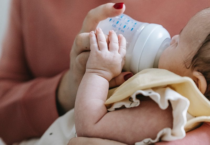 Mother feeding baby with baby bottle during formula shortage