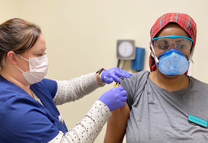 Woman with a facemask getting a Covid-19 vaccination by a nurse with a facemask